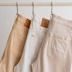 Trzy pary beżowych spodni wiszą na wieszakach. Idealne do letnich stylizacji, tworzą bazę dla wielu outfitów.
