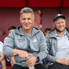 Marek Zub, trener Stali Rzeszów, z uśmiechem na twarzy, siedzi na ławce z butelką wody.