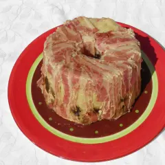 Un pâté en croûte de lard, une recette qui ne demande pas de farcement. Il est servi sur une assiette rouge décorée.