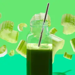 Ein Glas Selleriesaft mit einem Strohhalm, umgeben von schwebenden Selleriestücken. Die Selleriesaft Wirkung wird hier visuell dargestellt.