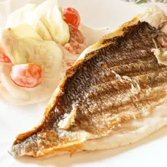 Dorada z grilla z chrupiącą skórką, podana z sałatką z pomidorków i ogórka w kremowym sosie.