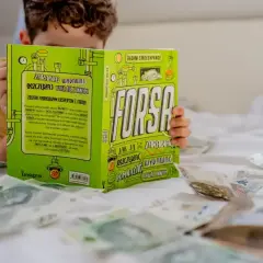 Chłopiec czyta książkę "Forsą. Jak zarabiać, oszczędzać, wydawać", rozłożoną na łóżku wśród pieniędzy. Czy pieniądze dają szczęście? Przykłady z literatury.