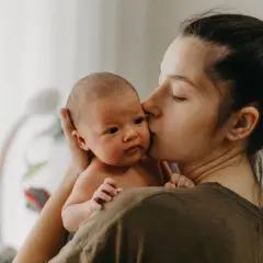 Mutter küsst ihr Neugeborenes. Die zarte Umarmung symbolisiert die Liebe und Geborgenheit, die in der **Wochenbett Dauer** so wichtig ist.