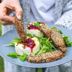 Ręka zanurza chrupiący sucharek w grillowanym serze z konfiturą. Czy takie sucharki są kaloryczne? Zależy od składu, ale te pełne ziaren wyglądają zdrowo!