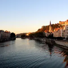 Vue de Lyon au coucher du soleil, avec le Rhône et ses quais bordés d'immeubles. La descente du Rhône offre un spectacle paisible.