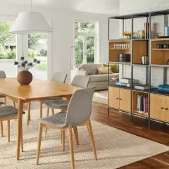 Open living and dining room ideas: a light wood table with grey chairs, a modern shelving unit, and a sofa visible through French doors.