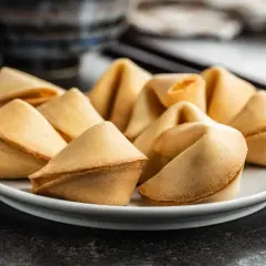 Talerz pełen złotych ciasteczek z wróżbą, ułożonych na ciemnym tle.