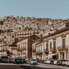 Cars navigate a steep, narrow street in a Sicilian town. Driving here might be challenging, but the views are worth it!