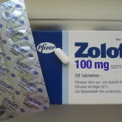 Opakowanie leku Zoloft 100 mg, zawierające 28 tabletek sertraliny. Obok znajduje się blister z lekami.
