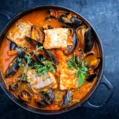 Una ricca zuppa di pesce in una pentola di ghisa, con pezzi di pesce bianco, cozze e erbe aromatiche fresche.