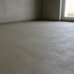 Świeżo wylana, szara wylewka cementowa na podłodze w pomieszczeniu z oknem.