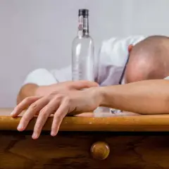 Bezwładne ciało na stole, pusta butelka obok. To obraz myślenia alkoholika, który stracił kontrolę nad swoim życiem.