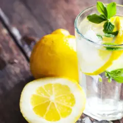 Erfrischendes zitronen wasser mit Eis und Minze, daneben ganze und halbierte Zitronen auf rustikalem Holz.