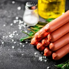 Świeże parówki ułożone na ciemnym tle, obok gałązki rozmarynu, soli i butelki oleju. Czy parówki można mrozić? Tak, można je mrozić.