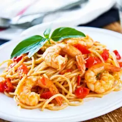 Un piatto invitante di pasta con gamberetti e pomodorini, guarnito con basilico fresco.