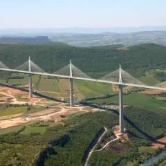 Najwyższy most w Europie, Viadukt Millau, przecina zieloną dolinę z imponującymi pylonami i stalowymi linami.