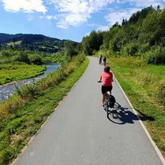 Rowerzyści przemierzają malowniczą trasę velo Krynica wzdłuż rzeki, otoczeni zielonymi wzgórzami i lasami.
