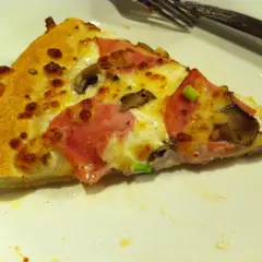 Kawałek pizzy z szynką i pieczarkami, idealny na festiwal pizzy, który trwa do jutra.