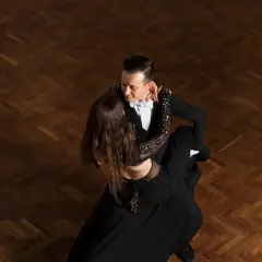 Para tańczy tango argentyńskie, wykonując skomplikowane kroki na drewnianym parkiecie.