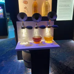 Tre flaskor med olika färger av sprit står upplysta på en hylla. En utställning på Vin & Sprit Museum.