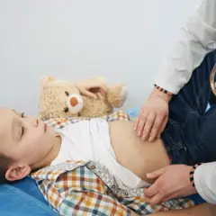 Lekarz bada brzuszek chłopca, który leży z pluszowym misiem. Może to być związane z objawami wyrostka u dzieci.