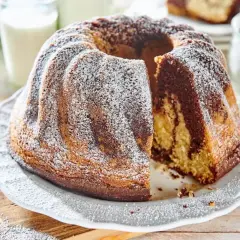 Puszysta babka na oleju z polewą z cukru pudru, z kawałkiem odciętym, by pokazać jej marmurkowe wnętrze.