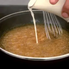 Se añade líquido a una salsa burbujeante en una sartén mientras se bate, para espesar salsa con maicena.