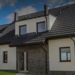Nowoczesny biały dom z szarym dachem i kamienną elewacją pod błękitnym niebem.