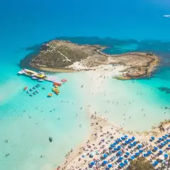 Widok z lotu ptaka na turkusową zatokę z plażą, leżakami i ludźmi kąpiącymi się w morzu.