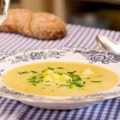 Eine cremige Zucchini-Suppe mit frischer Petersilie in einer eleganten Schüssel, daneben ein Glas Weißwein und ein Brot.