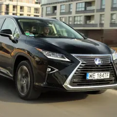 Czarny Lexus RX 450h jedzie ulicą w mieście, za nim widać nowoczesne budynki.