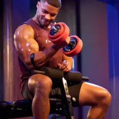 Mann mit Hantel beim Fitness-Training. Schweißglänzende Muskeln, konzentrierter Blick.