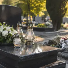 Białe kwiaty i znicze na nagrobku. Jak wyczyścić sztuczne kwiaty z cmentarza, by wyglądały jak nowe.