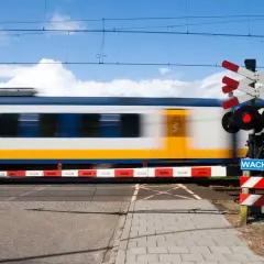 Pędzący pociąg mija przejazd kolejowy z czerwonym światłem i znakiem "Wacht". Widoczny jest charakterystyczny krzyż Andrzeja.