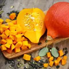 Pomarańczowa dynia hokkaido, pokrojona w kostkę i w całości, z pestkami i listkami szałwii. Idealna do uprawy i pysznych potraw.