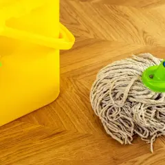 Cubo amarillo con paño verde y una mopa o fregona lista para limpiar el suelo de madera.