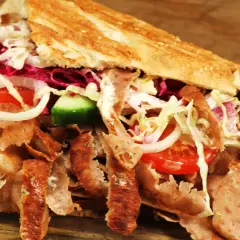 Kebab z mięsem, warzywami i sosem w bułce na drewnianym tle.