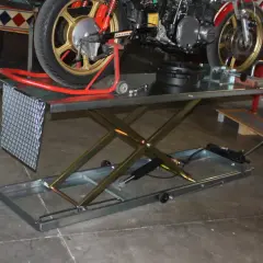 Moto su sollevatore a forbice. Il cerchio dorato della ruota posteriore, con finitura anodizzata, brilla sotto la luce.