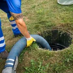 Pracownik w niebieskim kombinezonie wkłada wąż do szamba, co jest kluczowe, by wiedzieć, jak zrobić odpowietrzenie szamba.