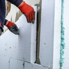 Rękawice ochronne i taśma miernicza towarzyszą pracy nad tym, jak przykleić styropian do płyty OSB. Widać klej i piankę montażową.