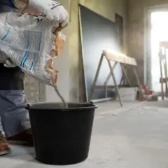 Budowlaniec wsypuje mieszankę do wiadra, przygotowując beton na styropianie. Kluczowa jest minimalna grubość wylewki betonowej na styropianie.
