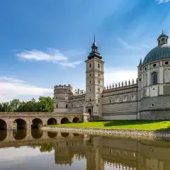 Zamek w Krasiczynie, majestatyczna budowla z wieżą i kopułą, odbija się w spokojnej tafli wody.