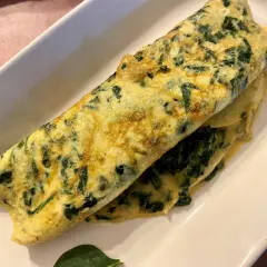 Une omelette aux épinards, dorée et moelleuse, servie sur une assiette blanche. Un délice simple et sain.