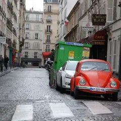 Une rue pavée à Paris, avec une Coccinelle rouge garée. Un panneau "parking gratuit Paris" serait le bienvenu ici.