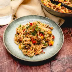 Ein Teller mit kritharaki salat mit hackfleisch, garniert mit frischen Kräutern. Bunte Paprikawürfel und Hackfleisch sind unter die Nudeln gemischt.