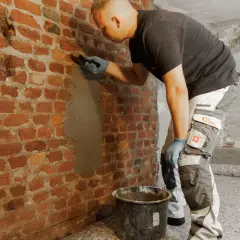 Mann verputzt feuchte Kellerwand.