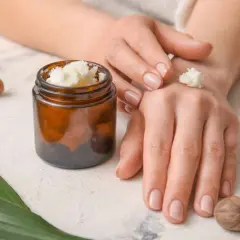 Mani che applicano burro di karitè, con noccioli e un barattolo. Informazioni su burro di karitè: controindicazioni.