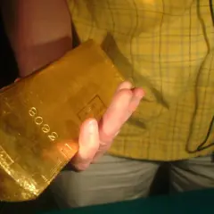 Dłoń trzyma błyszczącą sztabkę złota 5kg z wybitym numerem seryjnym.