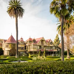 La casa Winchester, una mansión victoriana de colores vivos, se alza entre palmeras y jardines cuidados.