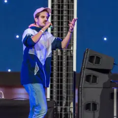 Artysta na scenie, jeden z najpopularniejszych polskich wykonawców pop, śpiewa do mikrofonu. W tle DJ przy laptopie.